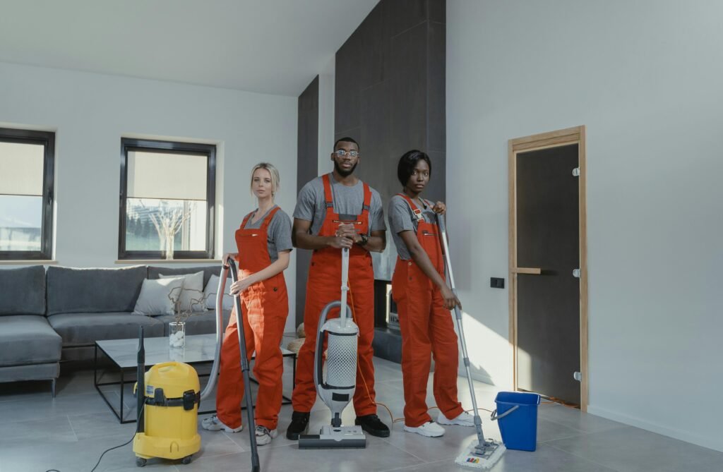 Diverse cleaning team in red uniforms ready to sanitize a modern living room with vacuum and mop.